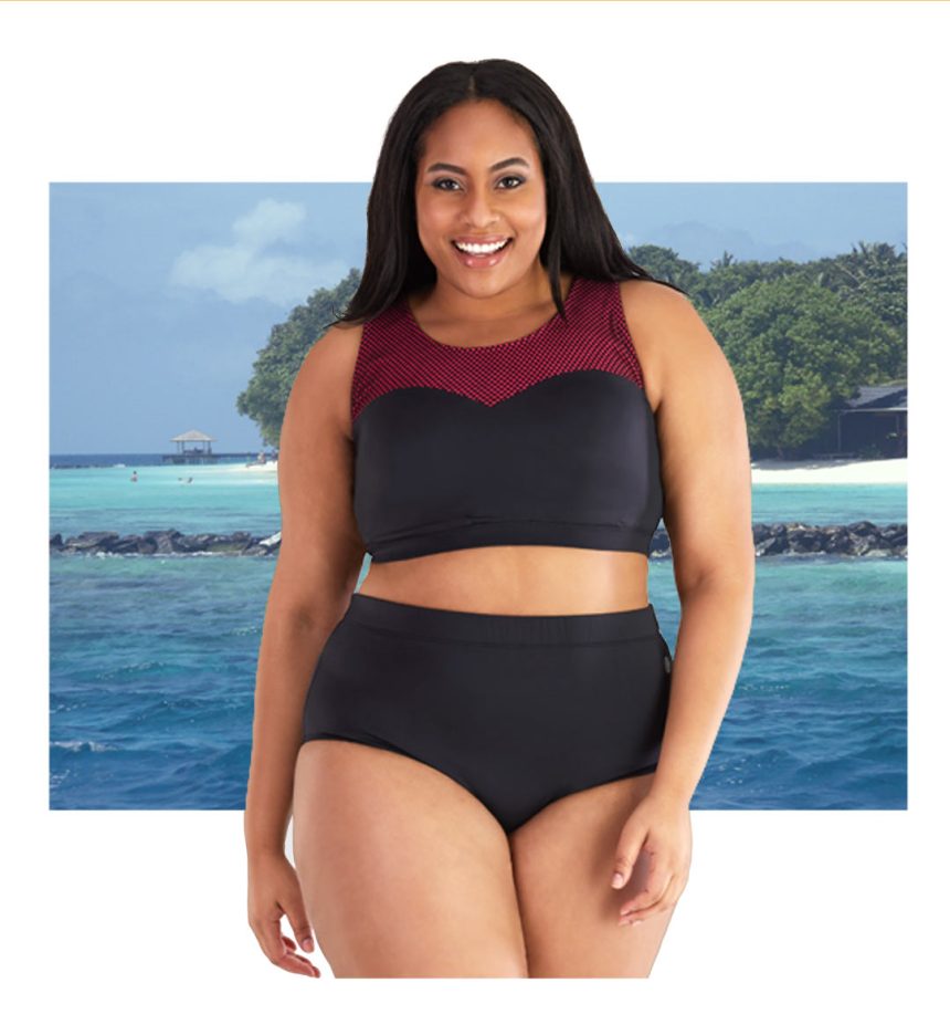 Plus size woman wearing red and black JunoActive swim bra with mesh strap and black swim briefs. The background is the ocean.