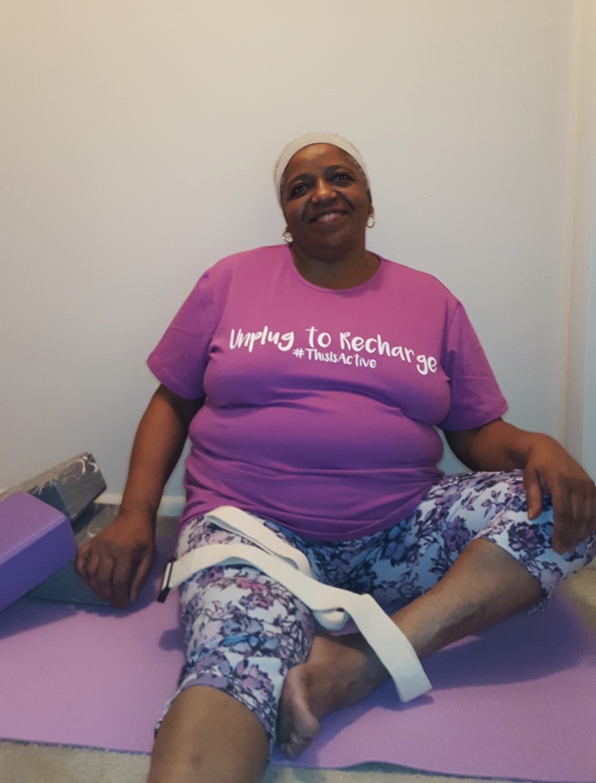 Plus size woman sitting on floor with yoga accessories wearing purple JunoActive plus size tee.